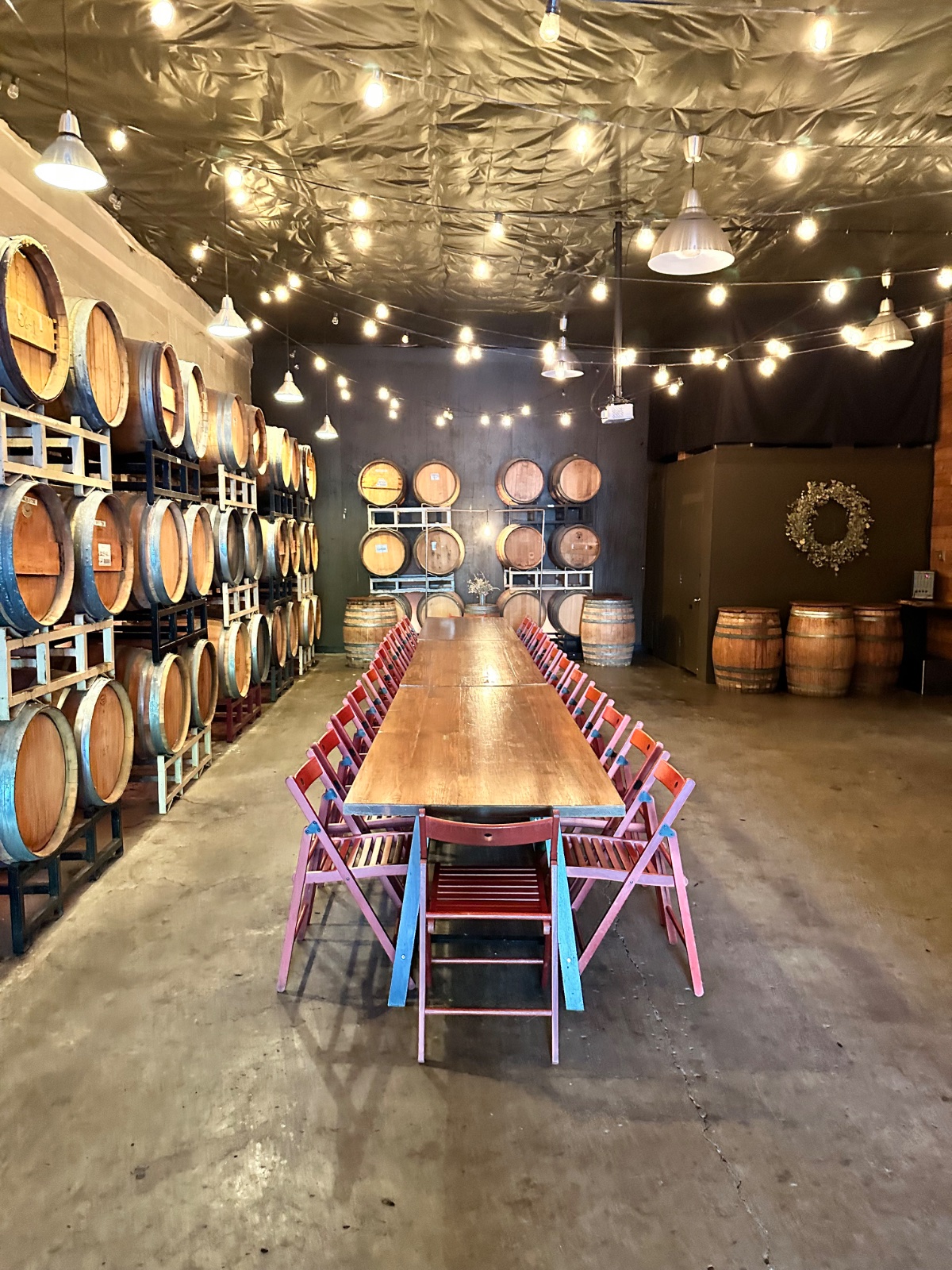 The ENSO barrel room: stacked oak barrels and a long farm table under strings of café lights