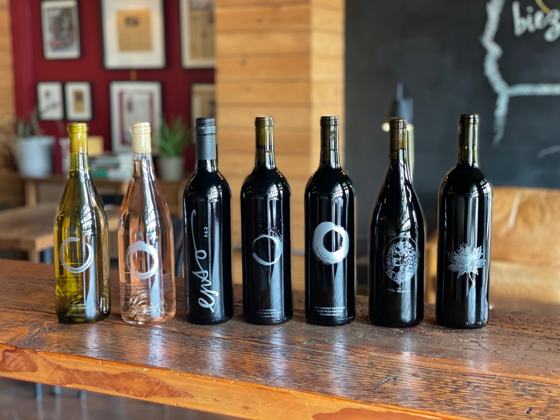Seven ENSO bottles lined up on the reclaimed-wood bar: white, rosé and five reds, each with its own etched label