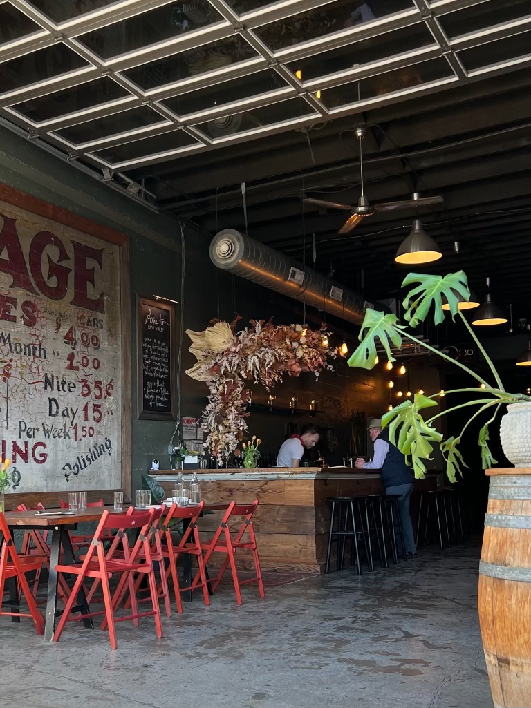 The ENSO space set with red folding chairs, the garage door open to the street and dried florals over the bar