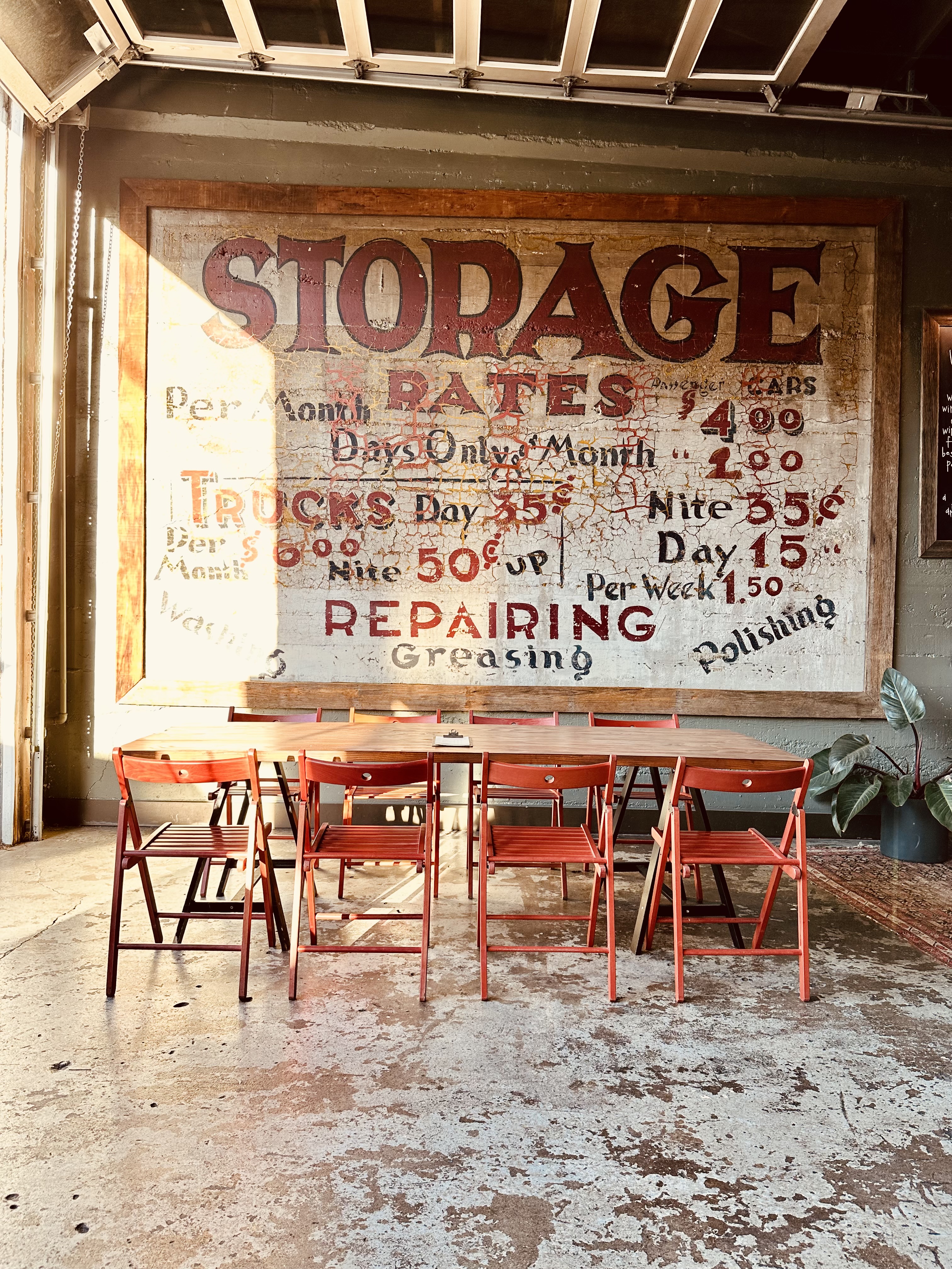 The original hand-painted Storage Rates mural on the garage wall, with a long table and red folding chairs in the sun
