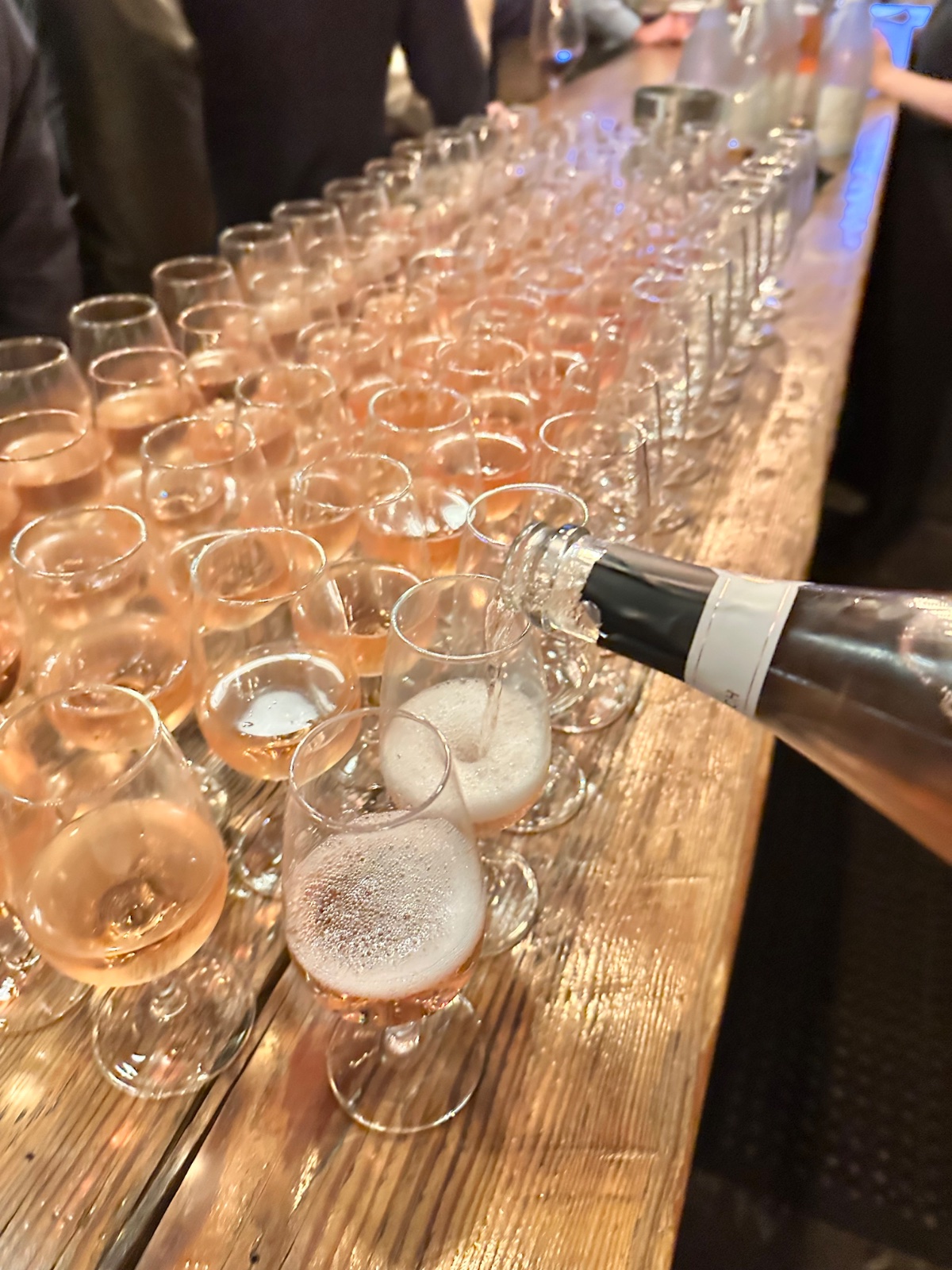 Sparkling rosé poured across dozens of glasses lined up along the ENSO bar