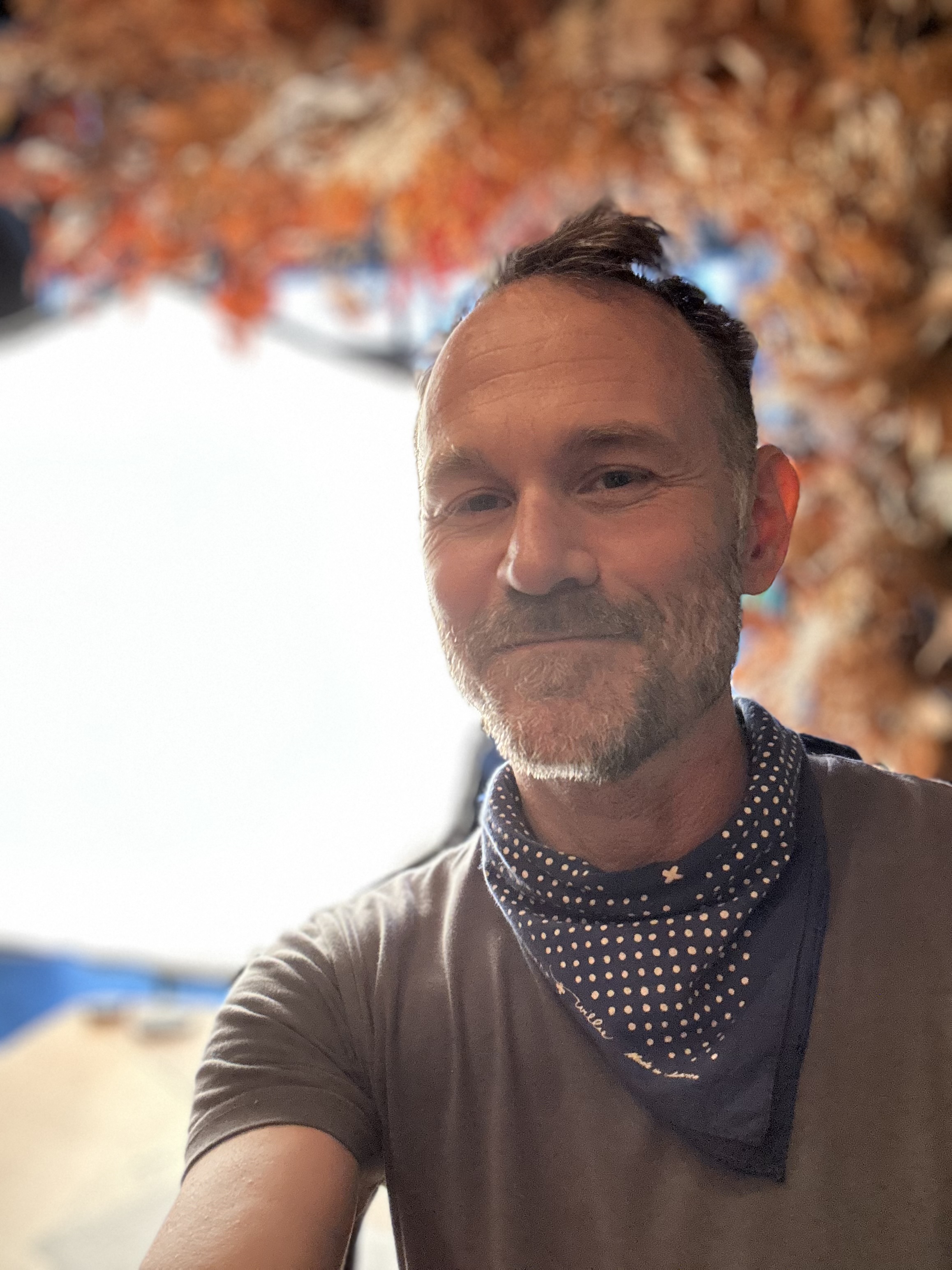 Ryan Sharp smiling in a polka-dot bandana beneath the dried-flower installation in the lounge