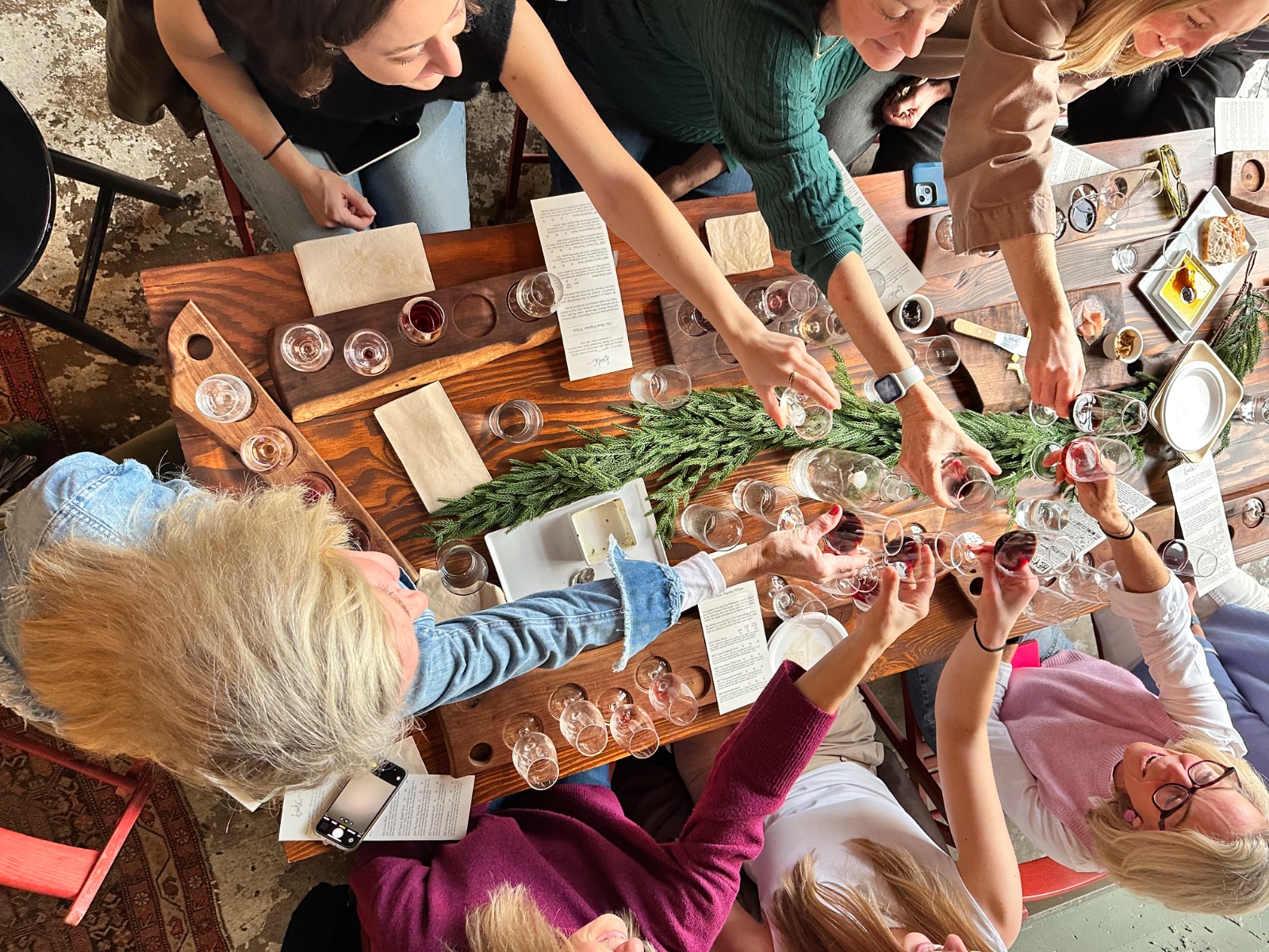 Friends reaching in for a toast over a long table of wine flights at ENSO