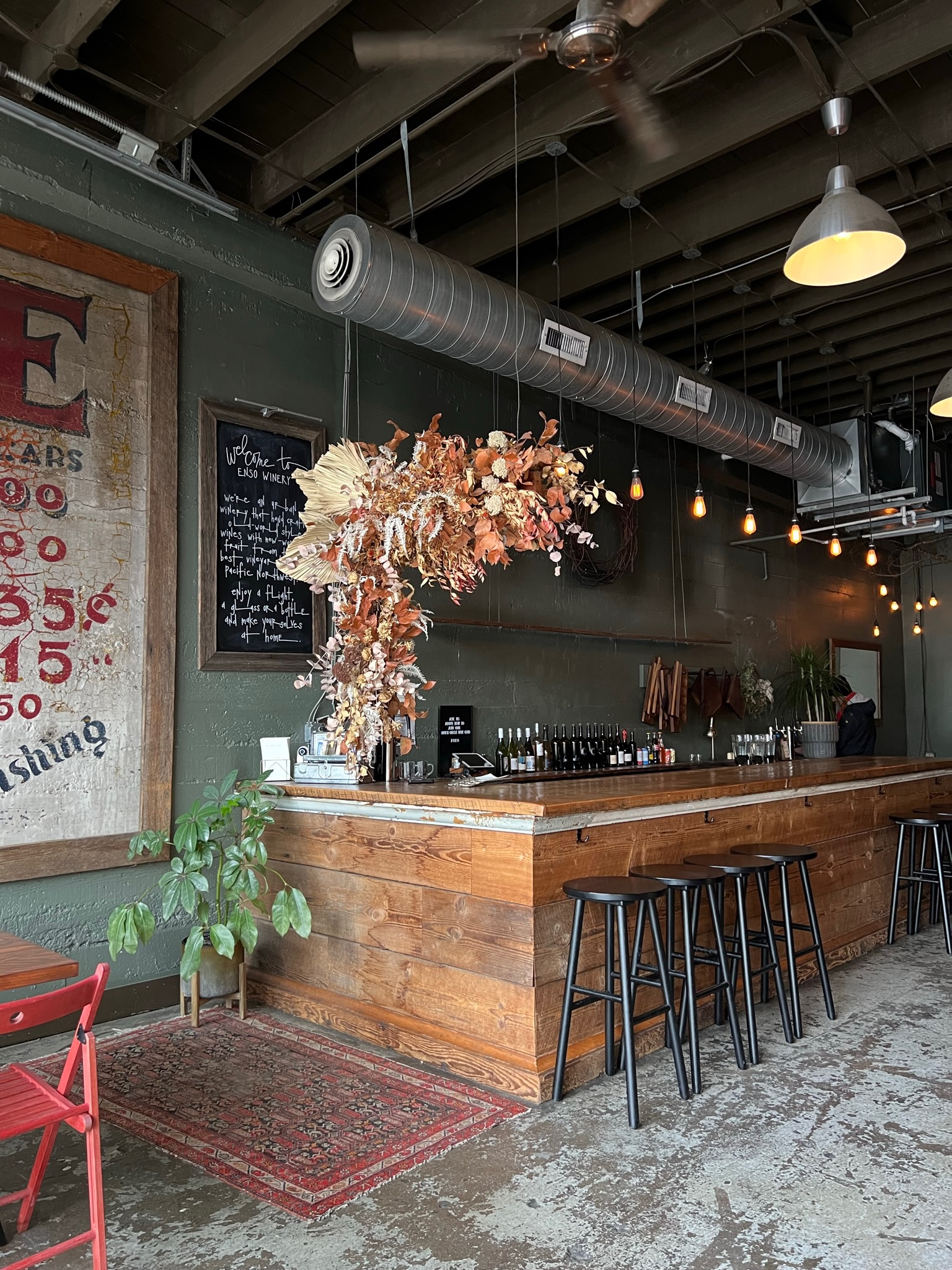 The ENSO wine bar beneath a cascade of dried florals, Edison bulbs glowing and stools waiting